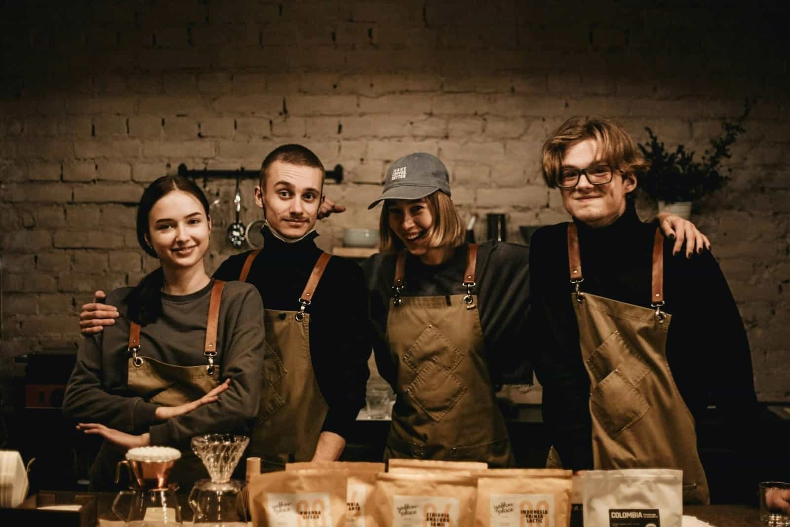 Cozy indoor portrait of four cheerful coffee shop employees in aprons, displaying teamwork.